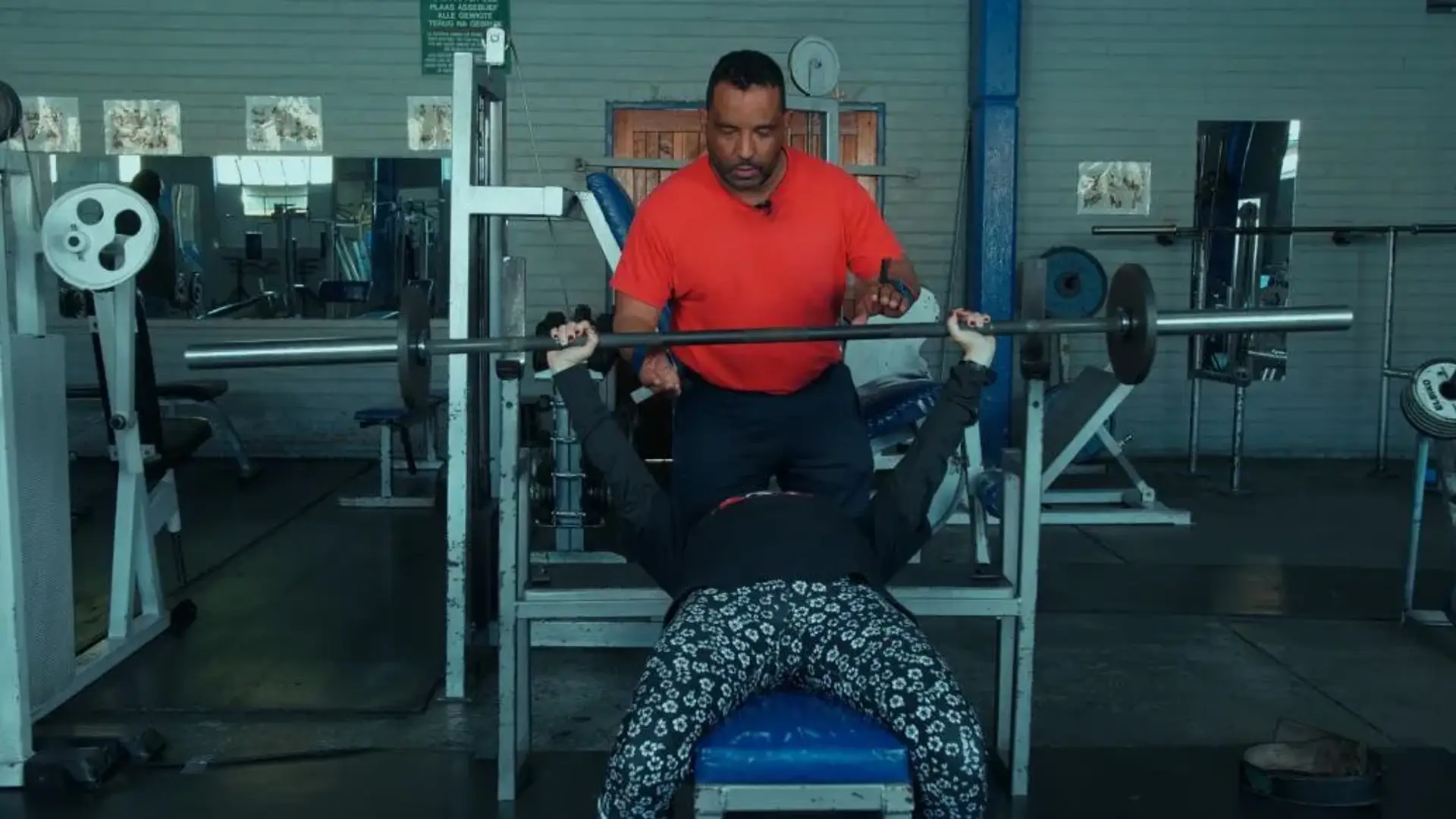 A man getting assisted with bench pressing by another man at the gym