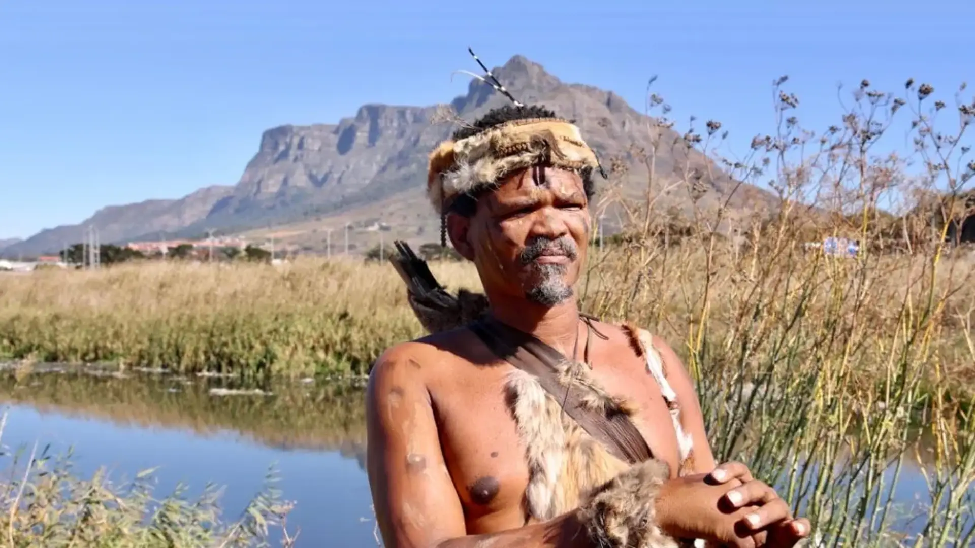 A Khoisan man wearing traditional attire in front of scenic landscape