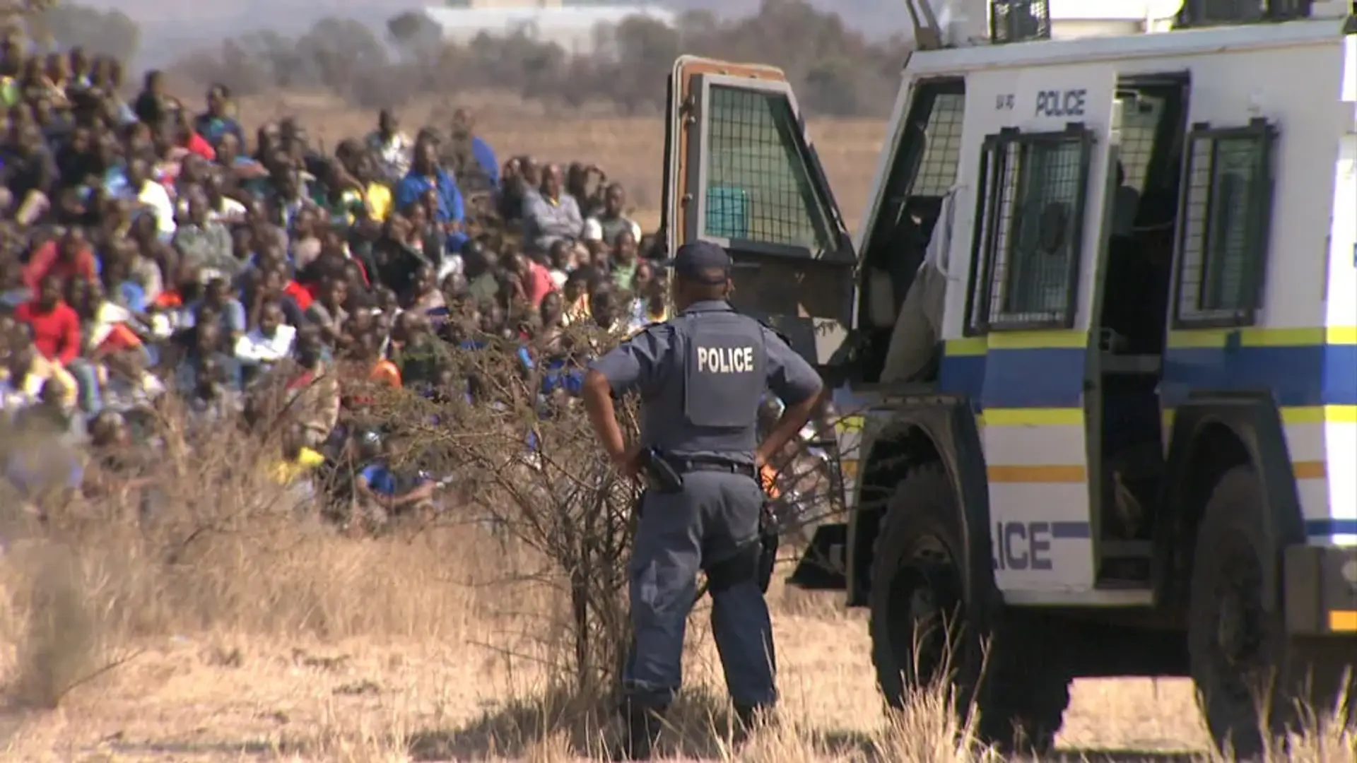 A police officer standing by a policy van while looking at a group of striking miners