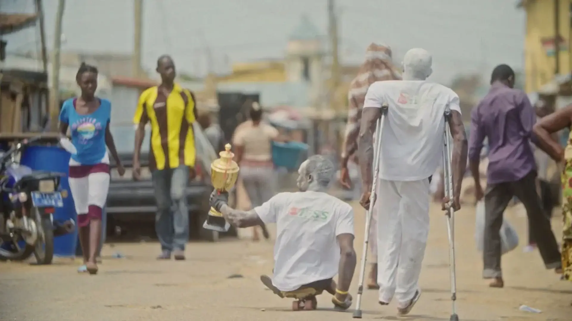 Two skate soccer players dressed in white walk down a street holding a trophy.