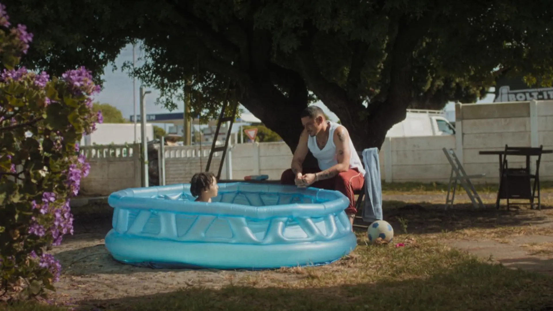 A man speaking to a child who is playing a plastic pool in a backyard